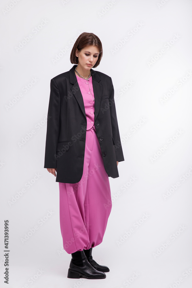 Fashion photo of a beautiful elegant young woman in a pretty oversize black jacket and pink suit, black boots posing over white background. Bob haircut. Studio Shot. White, black and pink colors Fashion photo of a beautiful elegant young woman in a pretty oversize black jacket and pink suit, black boots posing over white background. Bob haircut. Studio Shot. White, black and pink colors