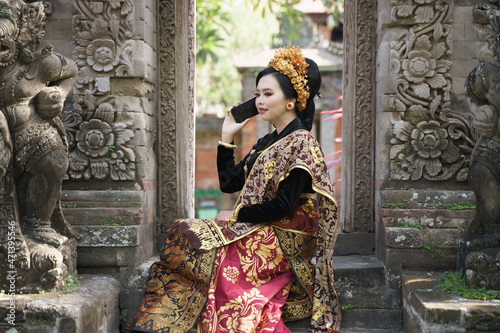 Woman wearing Balinese kebaya makes a call using a smartphone
