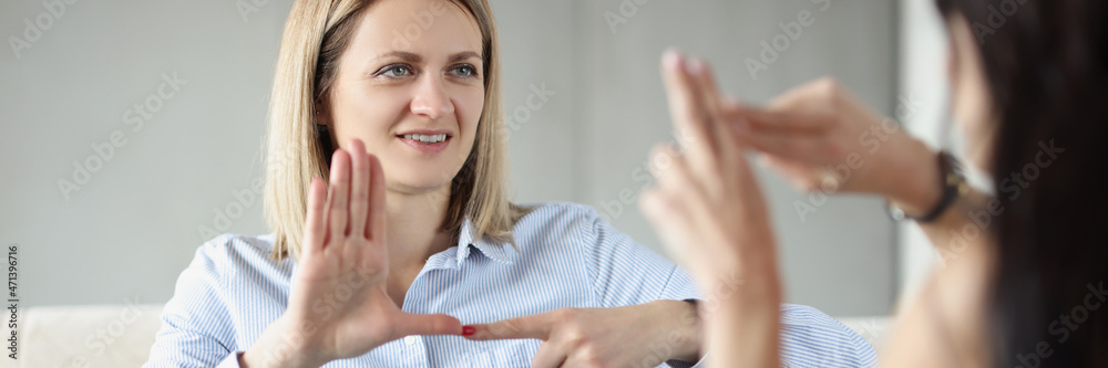 Naklejka premium Two young happy women sitting on couch and making sign languages