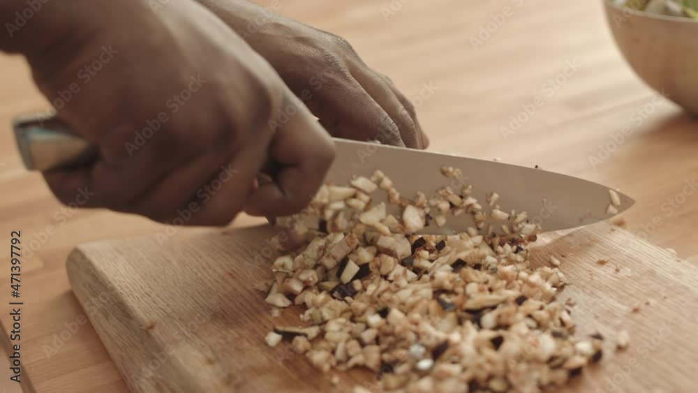 Close-up of unrecognizable person with hands in frame only cutting fresh eggplant with knife on cutting board into small pieces Close-up of unrecognizable person with hands in frame only cutting fresh eggplant with knife on cutting board into small pieces