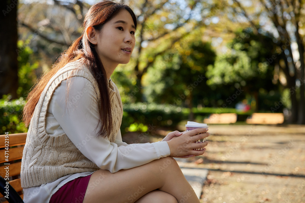 コーヒーカップを持ってベンチに座っているアジア人女性 コーヒーカップを持ってベンチに座っているアジア人女性