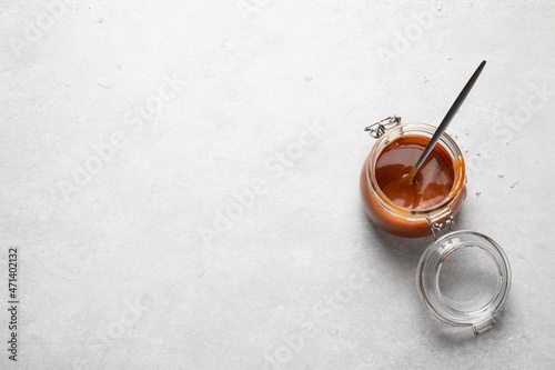 Homemade salted caramel sauce in glass jar on grey background. Copy space, top view.