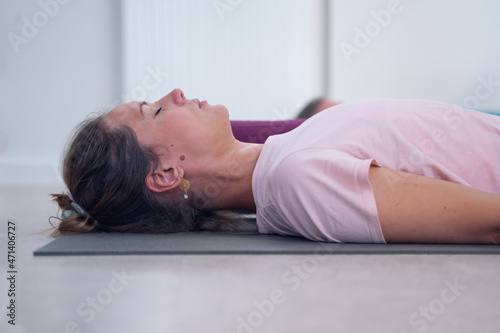 Side view of a woman, lying on a mat, breathing, during meditation in a yoga class.
