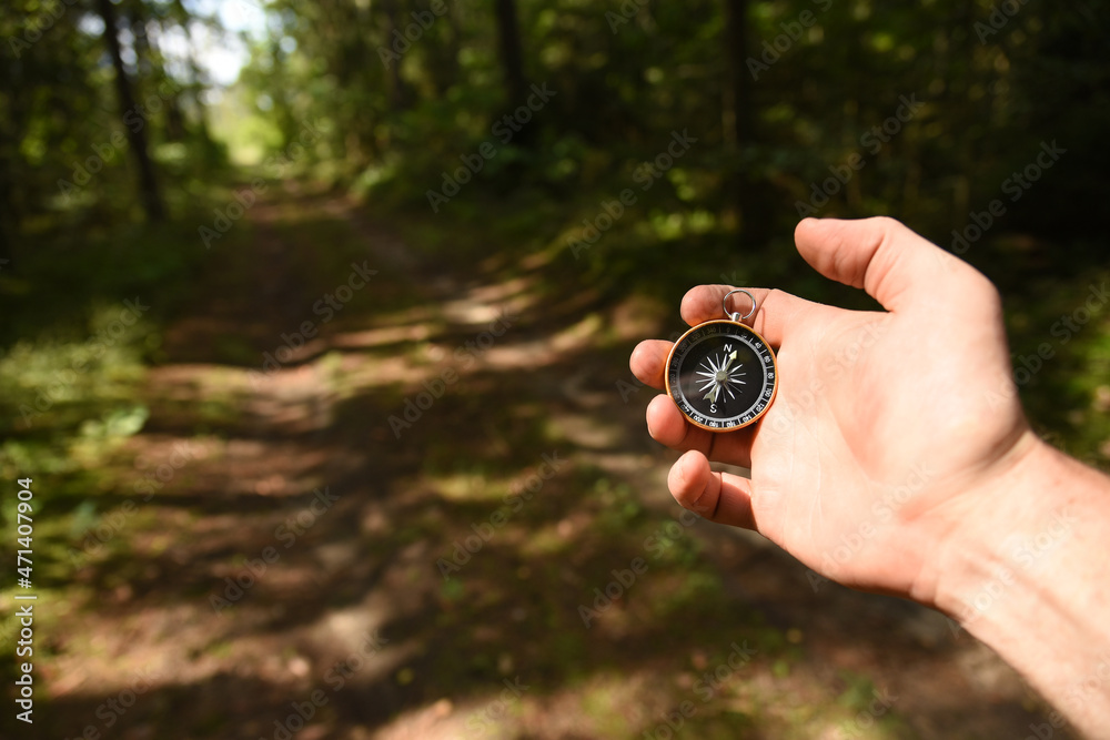 Compass in hand at forest. Tourist compass for orientation on the terrain. Magnetic declination сalculator. Historical explorer help. Map reading and land navigation concept. Orient on maps