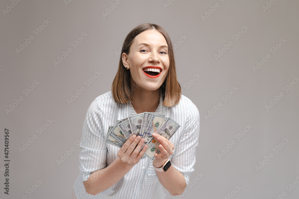 Photo of a surprised excited young girl isolated over gray background holding money make winner gesture. Photo of a surprised excited young girl isolated over gray background holding money make winner gesture.