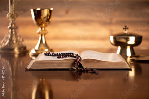 Catholic symbols composition. Religion concept. Holy Bible, rosary and golden chalice on the brown background. 