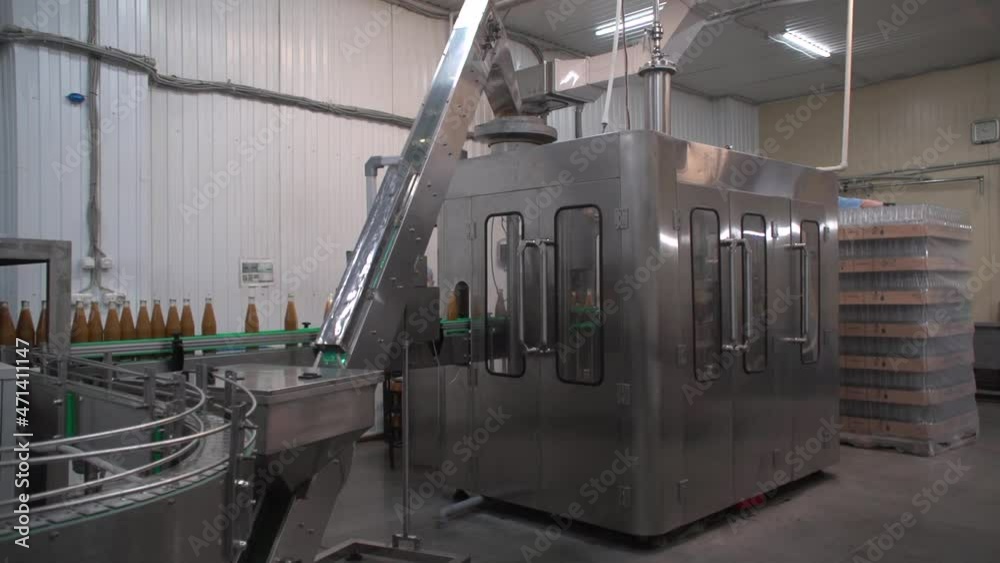 Medium shot of grey metallic bottling line. Orange-colored sea-buckthorn juice in glass bottles Medium shot of grey metallic bottling line. Orange-colored sea-buckthorn juice in glass bottles