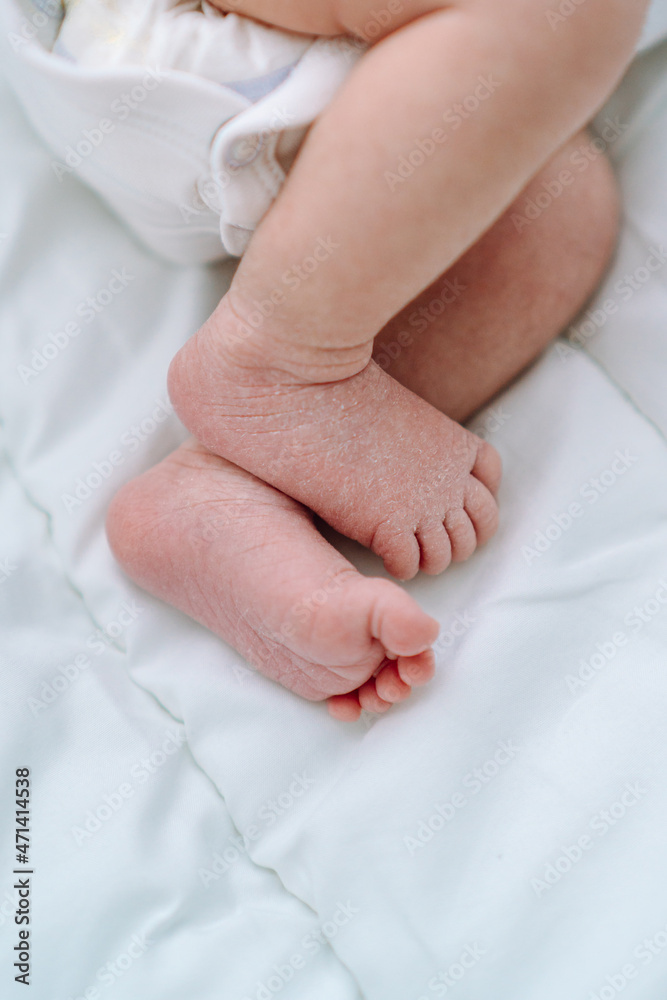 Close bare feet of newborn unrecognizable child in white clothes on light blanket. Skin care, baby care Close bare feet of newborn unrecognizable child in white clothes on light blanket. Skin care, baby care