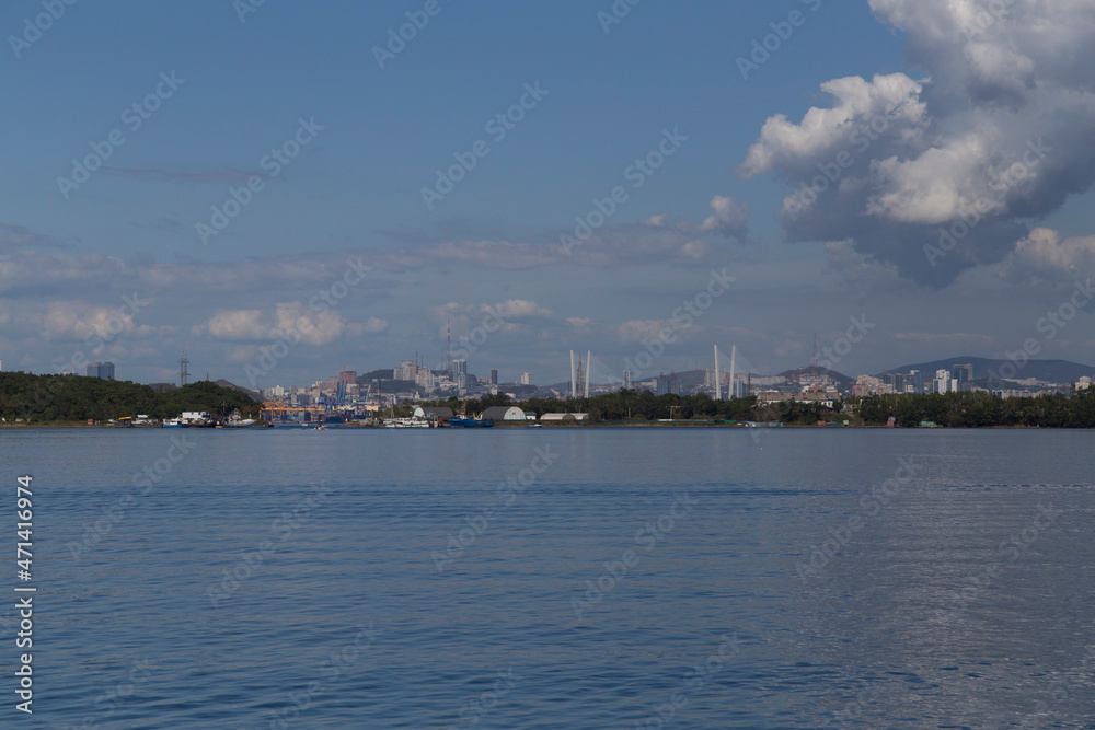 day view of the sea, islets, capes, white clouds and blue sky and the city on the hills in the background. Shot in the Novik harbor on island Russky in Vladivostok, Russia