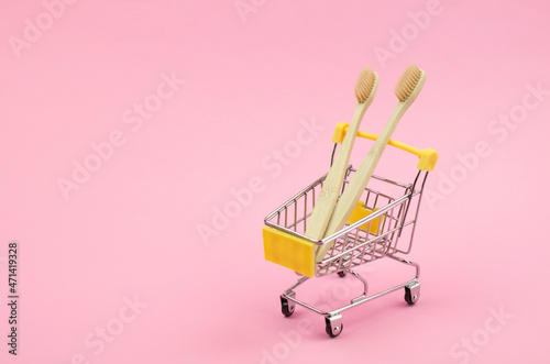 Two wooden toothbrushes in a shopping trolley on a yellow background