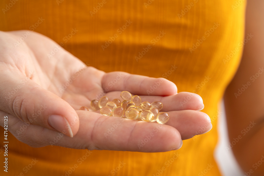 Closeup of woman hand and vitamin D capsules against bright yellow shirt.Concept of deficiency of vitamins Closeup of woman hand and vitamin D capsules against bright yellow shirt.Concept of deficiency of vitamins