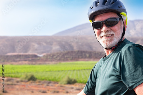 Senior man cyclist enjoying riding outdoors with his electro bike. Vineyard and mountains in background © luciano