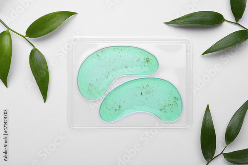 Fototapeta Package with under eye patches and green twigs on white background, flat lay