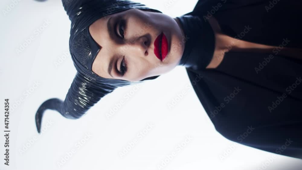 Make up woman in witch costume stands on white background in studio and looks forward, vertical video, front view. Woman cosplay witch for holiday