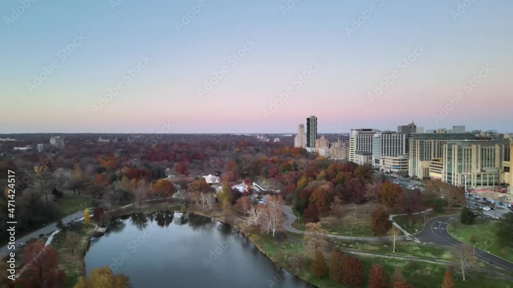 Pan drone shot of East side of Forest Park, St. Louis, MO.  Autumn season, colored trees with and buildings from the city during sunset