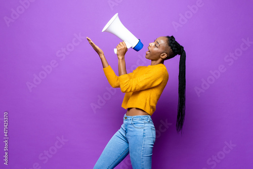African American woman speaking on megaphone and pointing hand up in isolated purple studio background