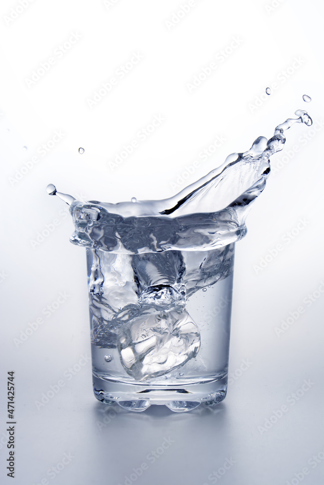 Glass of water with ice cube splashing.