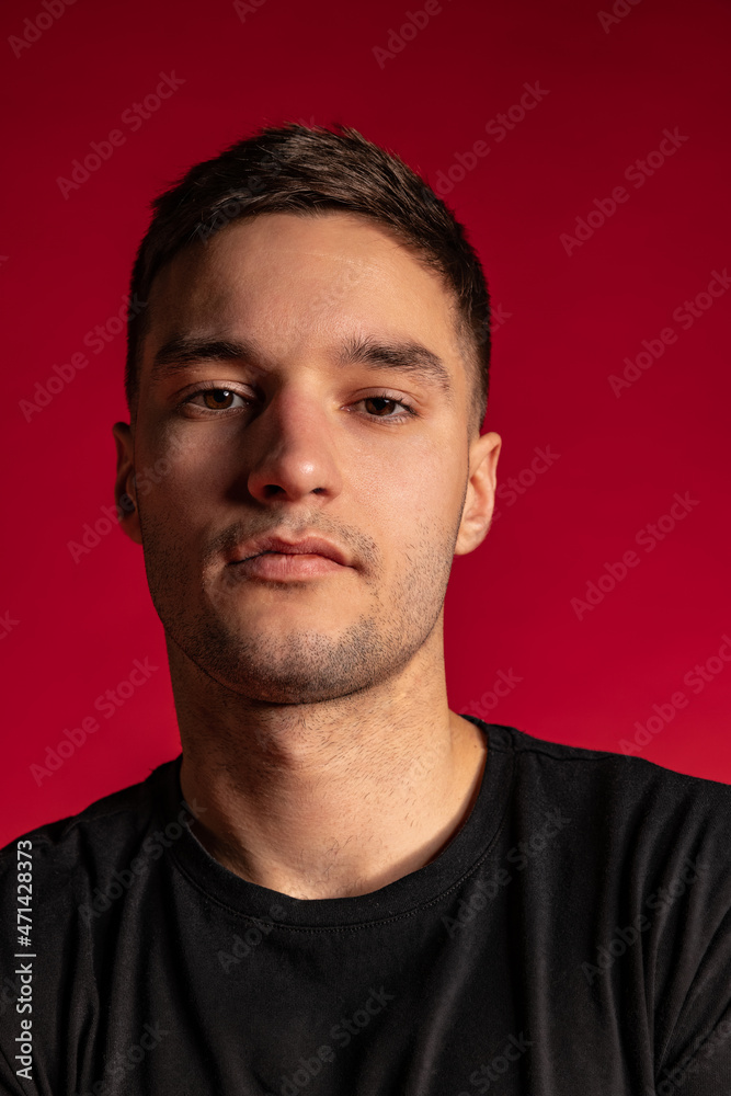 Close-up portrait of young handsome man in black t-shirt looking at camera isolated on dark red studio background. Close-up portrait of young handsome man in black t-shirt looking at camera isolated on dark red studio background.