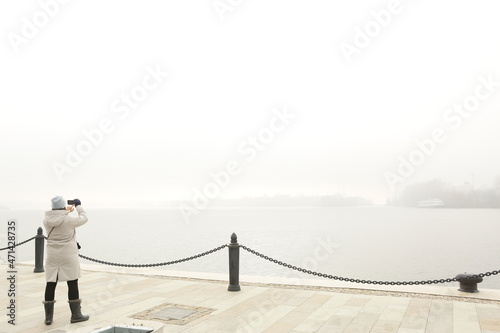 woman takes photo of foggy landscape of marina shore with boat on lake background High quality photo photo