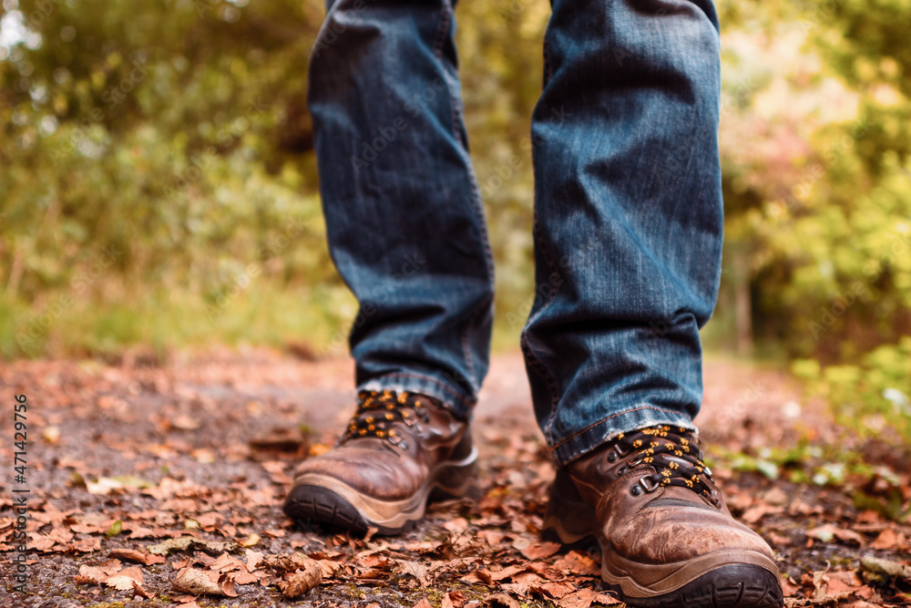 Old brown worn out hiking boots and blue jeans in a park. Selective focus. Outdoor adventure concept. Rugged lasting design.