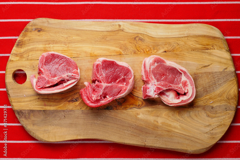 Three fresh lamb loin chops on a wooden board. Meat industry product, butcher craft and skill example.