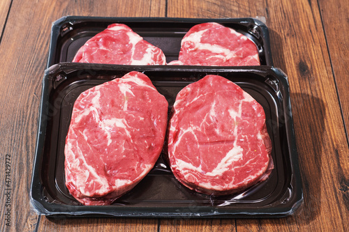 Rib eye steaks on a black plastic tray on a wooden table. Premium beef product. Fresh meat. Butcher craft. Food supply industry.
