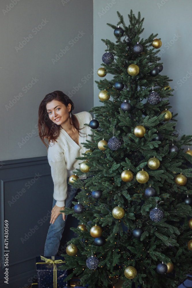 A beautiful girl is standing at the Christmas tree. New Year's mood. Merry Christmas A beautiful girl is standing at the Christmas tree. New Year's mood. Merry Christmas
