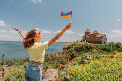 Fotografie Happy tourist woman with armenian flag posing at the Hayravank Monastery on the shore of Lake Sevan