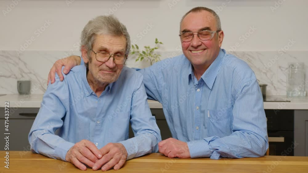 Portrait of the two Caucasian old men sitting, hugging and smiling to the camera in front of the camera at the house. Portrait of the two Caucasian old men sitting, hugging and smiling to the camera in front of the camera at the house.