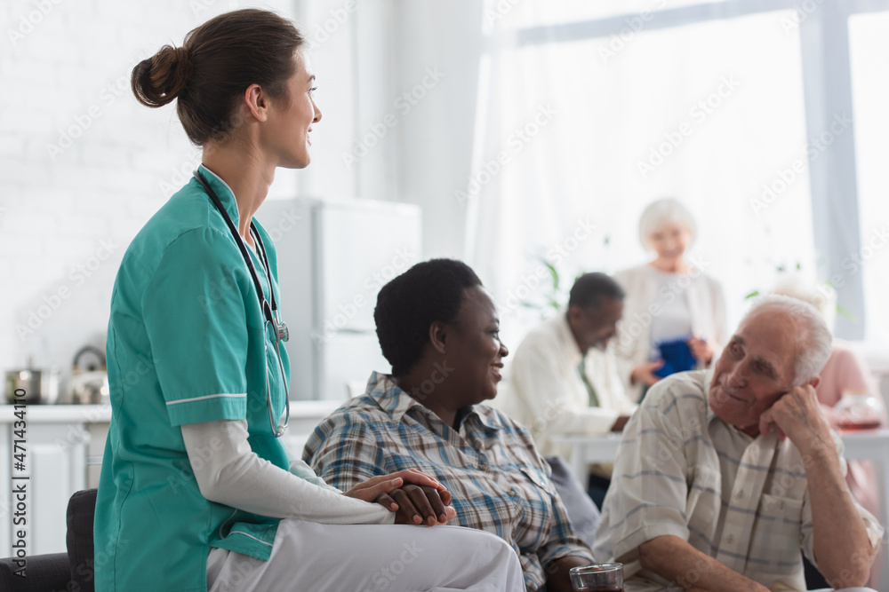 Young nurse holding hand of african american patient with tea in nursing home Young nurse holding hand of african american patient with tea in nursing home