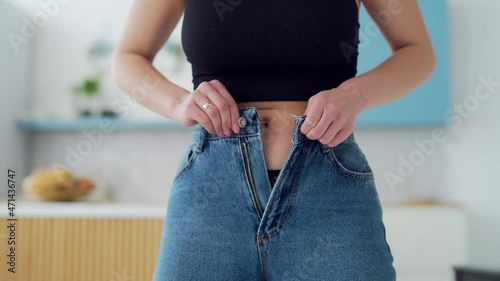 Young fat woman cannot wear small pants after gaining weight. An overweight female tries to button her jeans. Girl with belly getting dressed putting trousers on. Overweight trying to fasten too