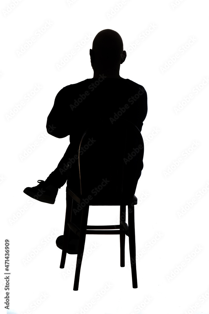 rear view of the silhouette of a man sitting on chair with casual clothes with his legs and arms crossed