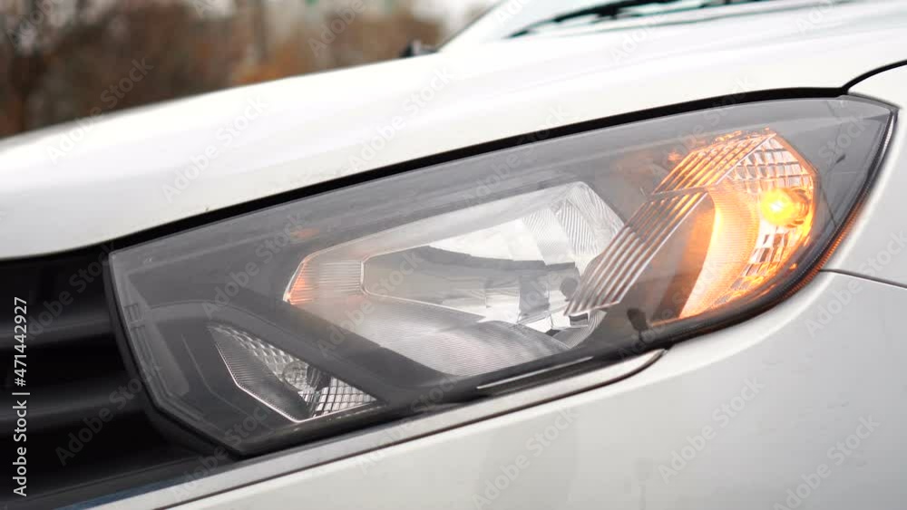 Headlight of gray car close-up with flashing turn signal. Car alarm on. Security signal. Headlight of gray car close-up with flashing turn signal. Car alarm on. Security signal.