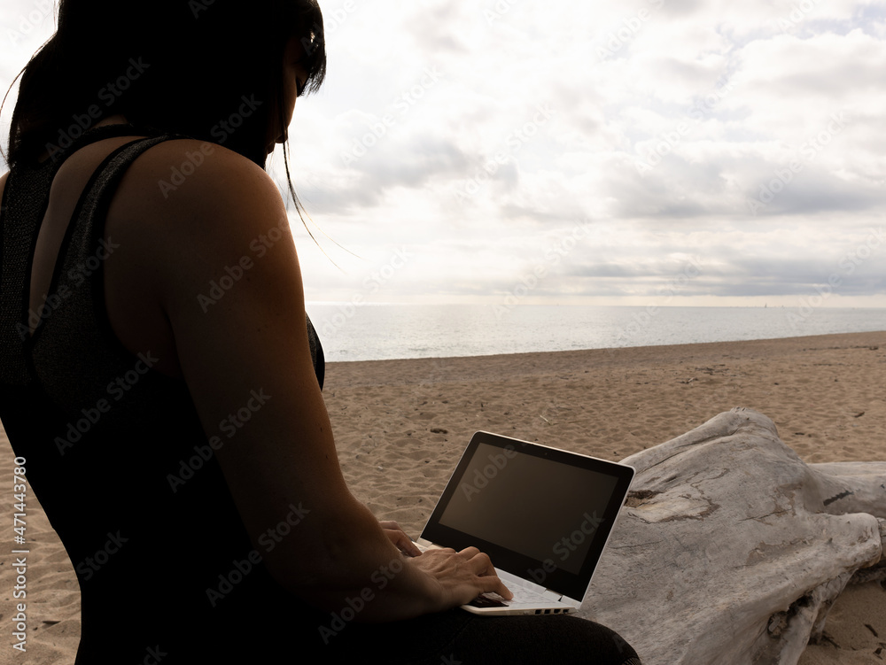 girl working with the computer on the beach at sunset