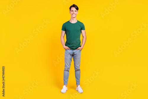 Full length photo of cheerful happy positive man hold hands pockets denim jeans isolated on yellow color background
