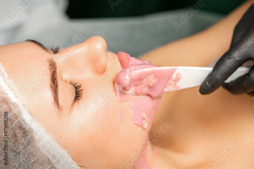 Beautician applying alginate peel-off powder facial mask with the spatula in a spa