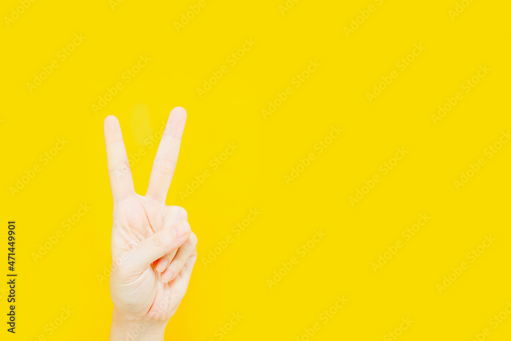 Woman's Hand gesture with V sign for victory or peace on a yellow background