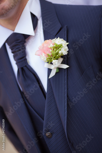 Close up groom in blue suit and blue vest and burgundy tie with a boutonniere of white and rose flowers. Man in suit expects bride on wedding day.