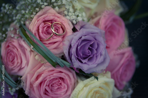 Top down view two golden wedding rings on pink rose bouquet flowers background with copy paste space