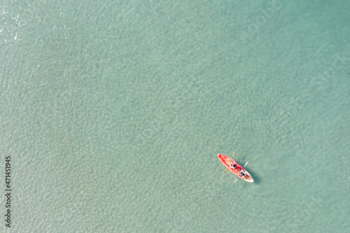 Aerial view of blue sea with couple and floating colorful kayak is going into sand beach, person with life jacket on boat.