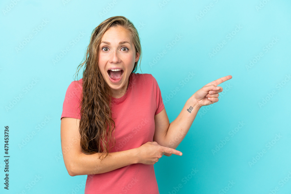 Young caucasian woman isolated on blue background surprised and pointing side Young caucasian woman isolated on blue background surprised and pointing side
