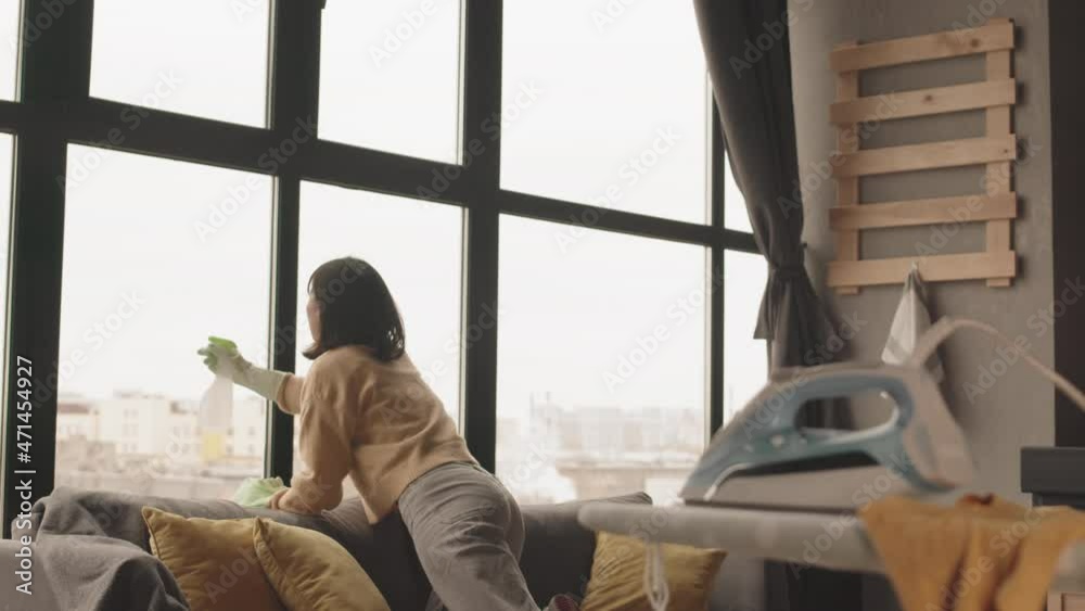 Slowmo shot of young Asian woman cleaning windows while doing housework at her apartment