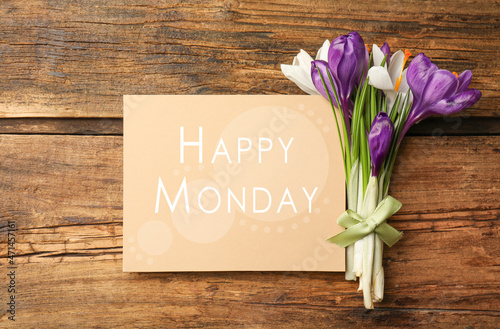 Beautiful spring crocus flowers and card with phrase Happy Monday on wooden table, flat lay