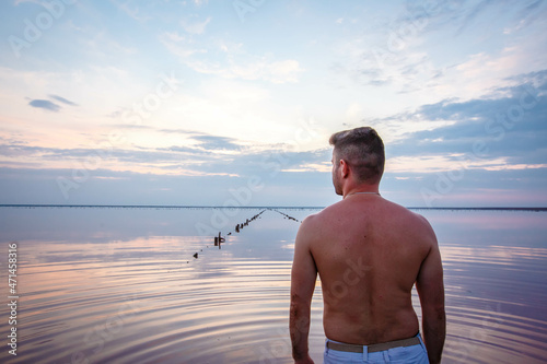 A young man, stripped to shorts, walks on a pink salt lake at sunset. Ukraine. Lemurian salt lake