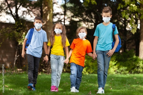 Group of schoolchildren in masks walking together on the park
