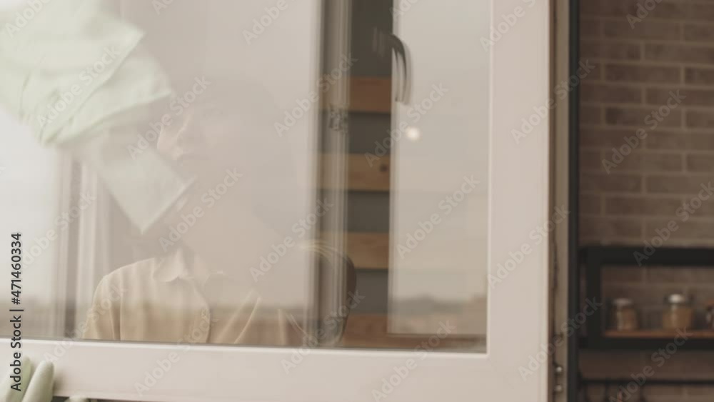 Chest up slowmo shot of young Asian woman cleaning windows at home using cloth