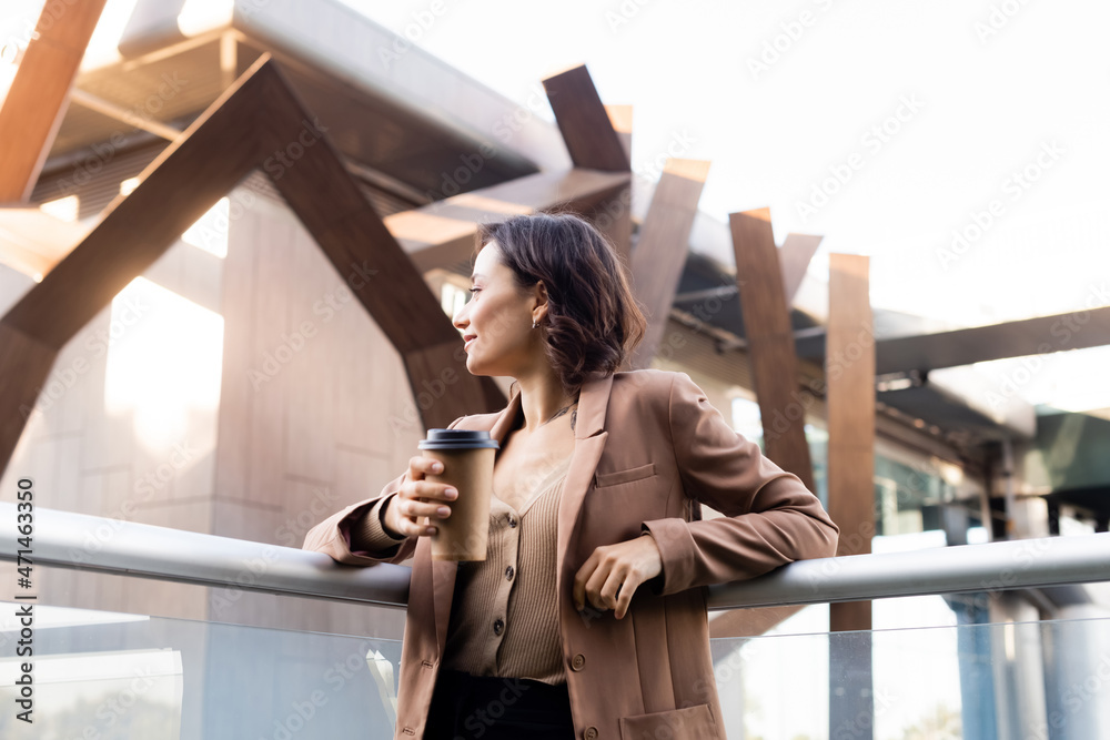 Fototapeta premium brunette woman in beige blazer looking away on balcony of building outdoors