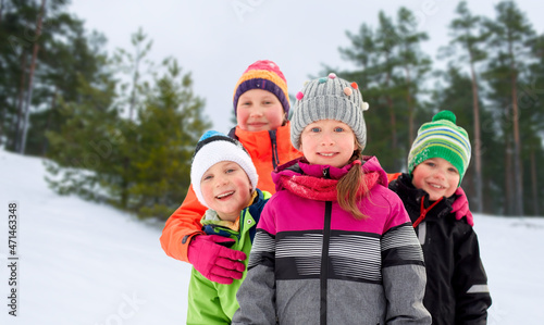 childhood, friendship and season concept - group of happy little kids in winter clothes outdoors over snowy forest or park background