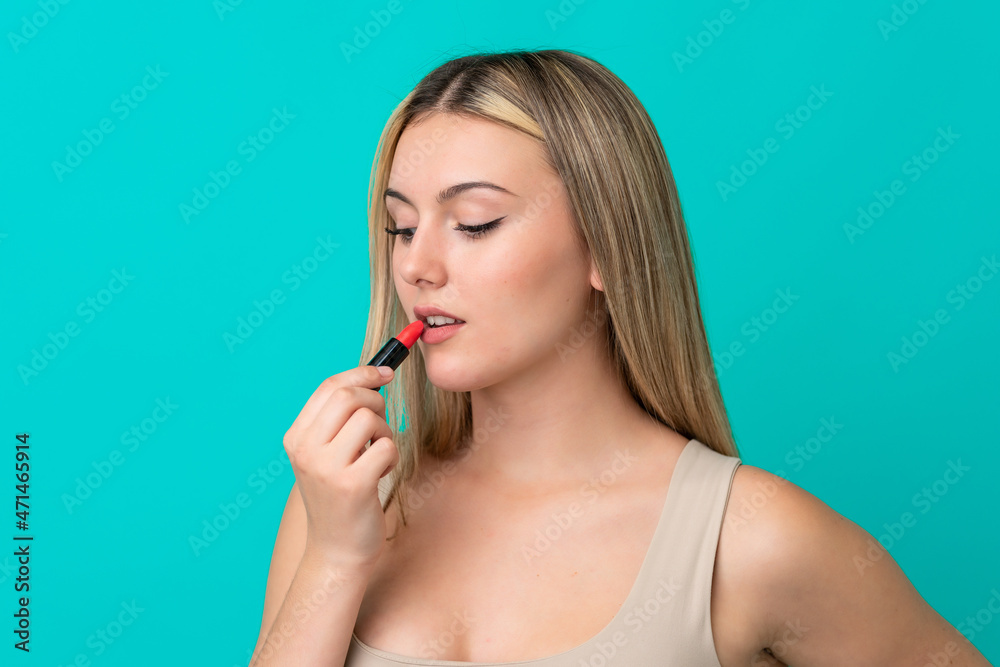 Young caucasian woman isolated on blue background holding red lipstick Young caucasian woman isolated on blue background holding red lipstick