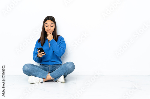 Young mixed race woman sitting on the floor isolated on white background thinking and sending a message